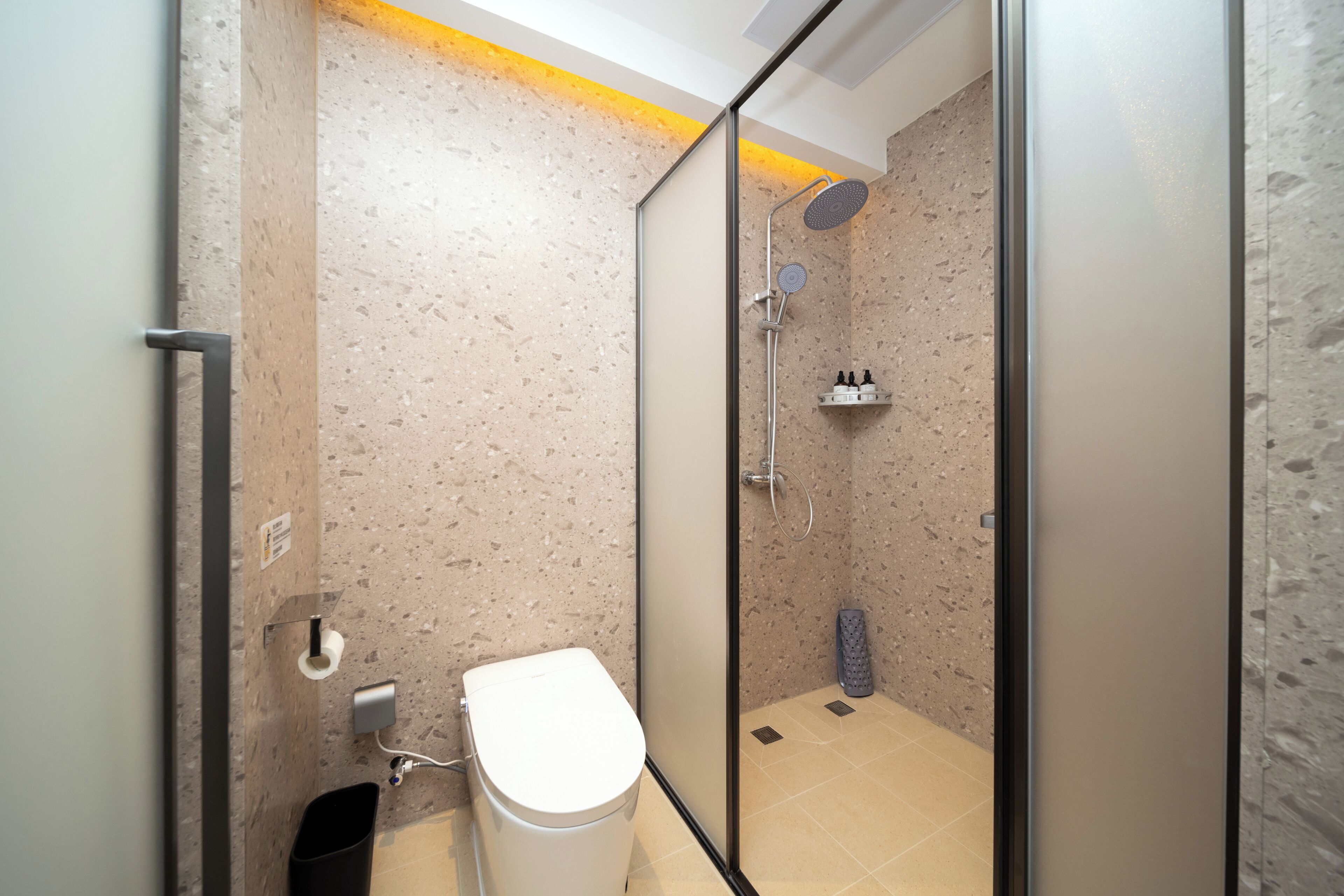 Ein modernes Badezimmer mit einer Duschkabine, einer Toilette und einem Ablagefach für Pflegeprodukte.