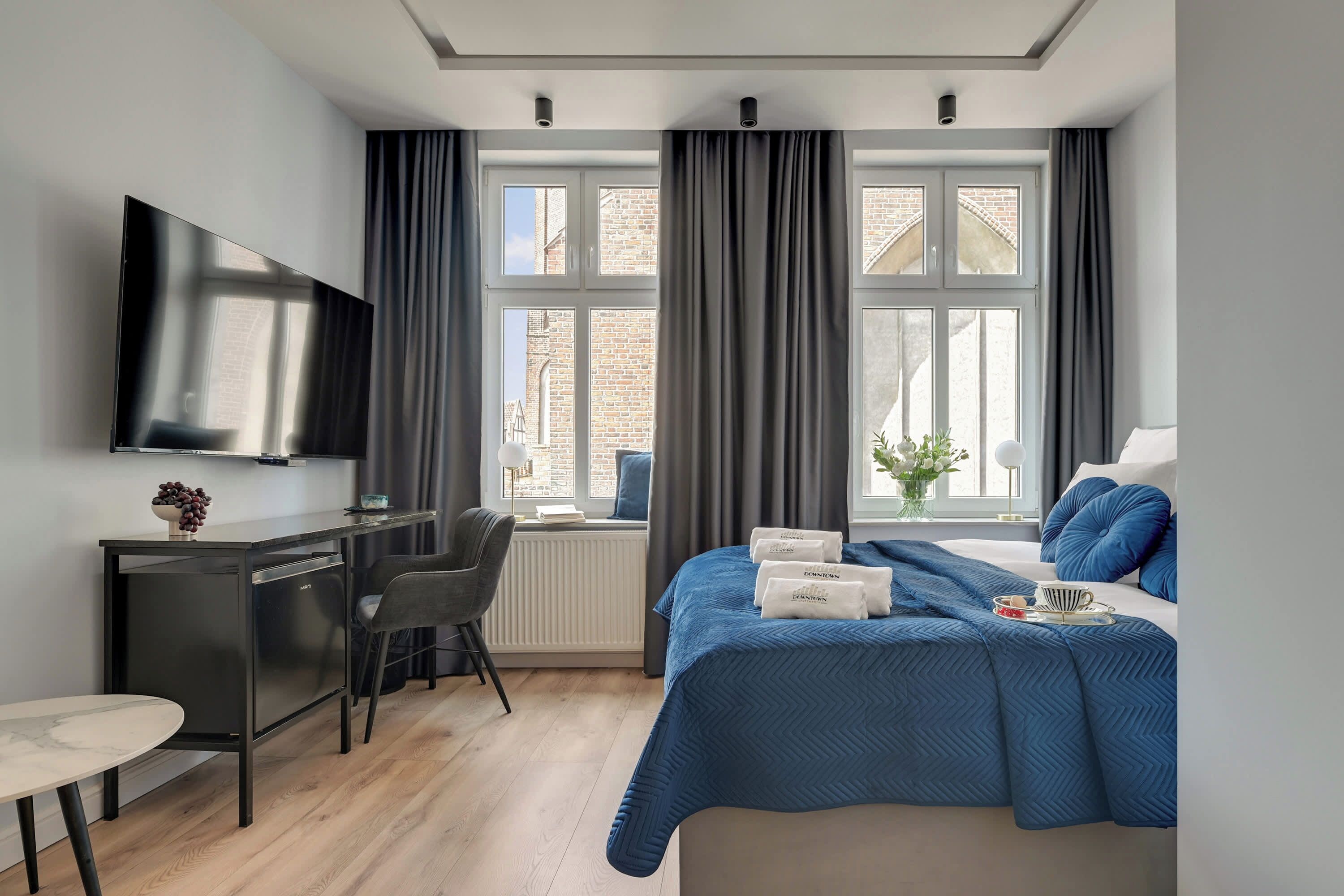 Habitación de hotel moderna con cama, escritorio, silla, televisor y ventanas amplias.