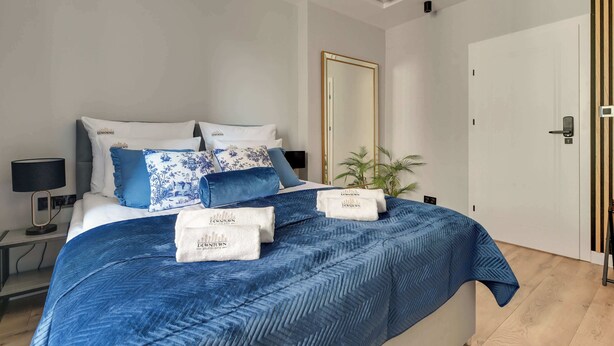 Ein modernes Hotelzimmer mit einem großen Bett, einem Nachttisch mit Lampe, einem Spiegel und einer Tür mit einer vertikalen Holzverkleidung.
