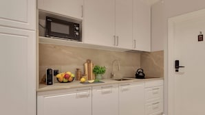 Una cocina moderna con armarios blancos, microondas, hervidor y frutero.