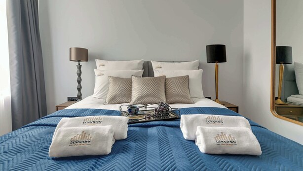 Habitación de hotel con cama, dos lámparas de noche, un espejo y una bandeja con una taza y uvas.