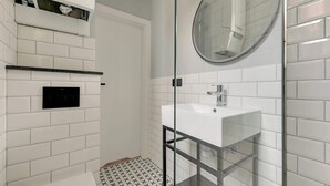 Un baño con ducha envuelta en vidrio, un lavabo blanco y un panel de control negro en la pared.