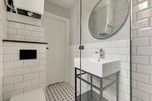Ein Badezimmer mit einer Duschkabine aus Glas, einem weißen Waschbecken und einem schwarzen Bedienfeld an der Wand.