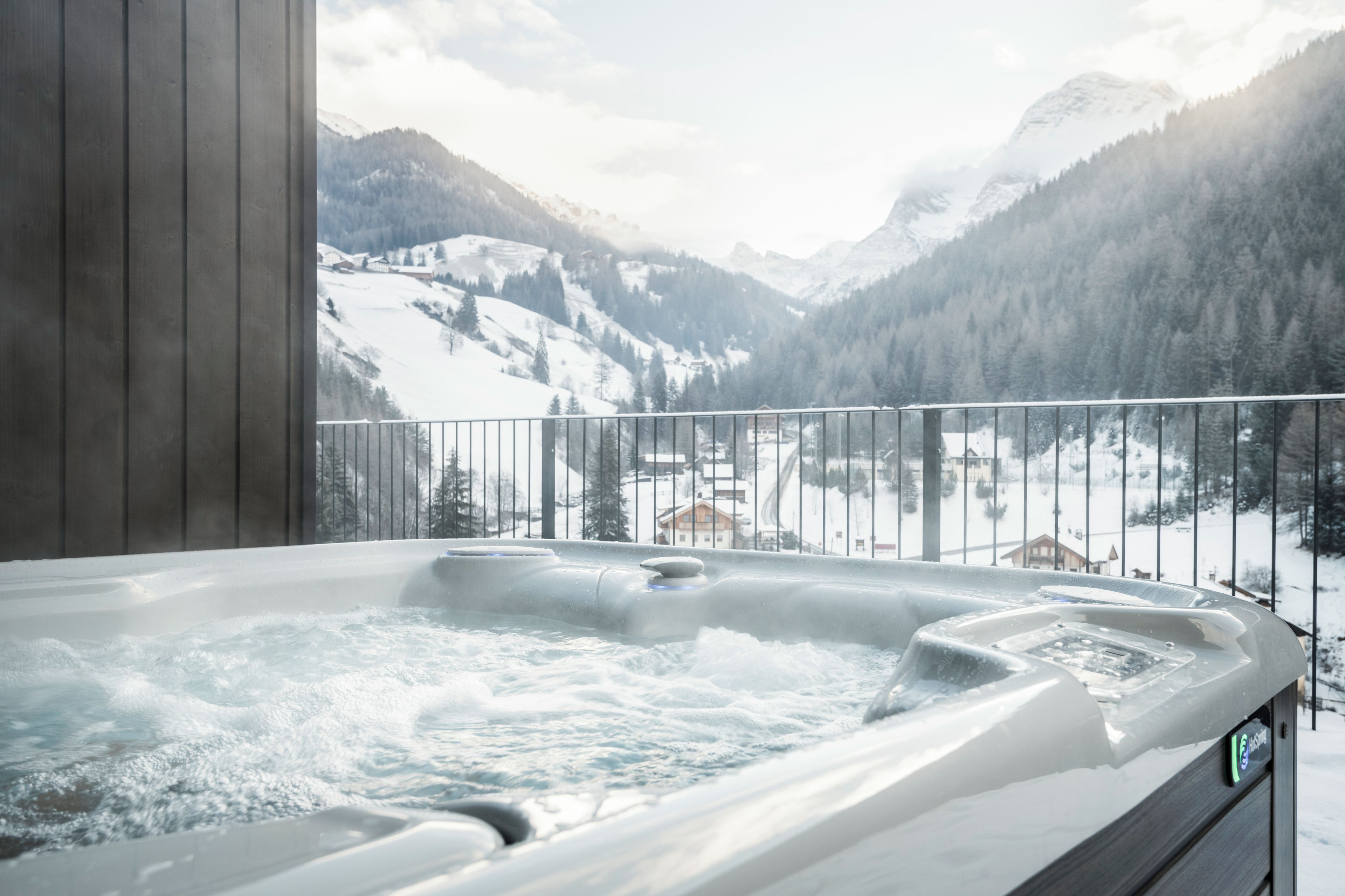 Ein Whirlpool mit Blick auf verschneite Berge und eine Holzterrasse.