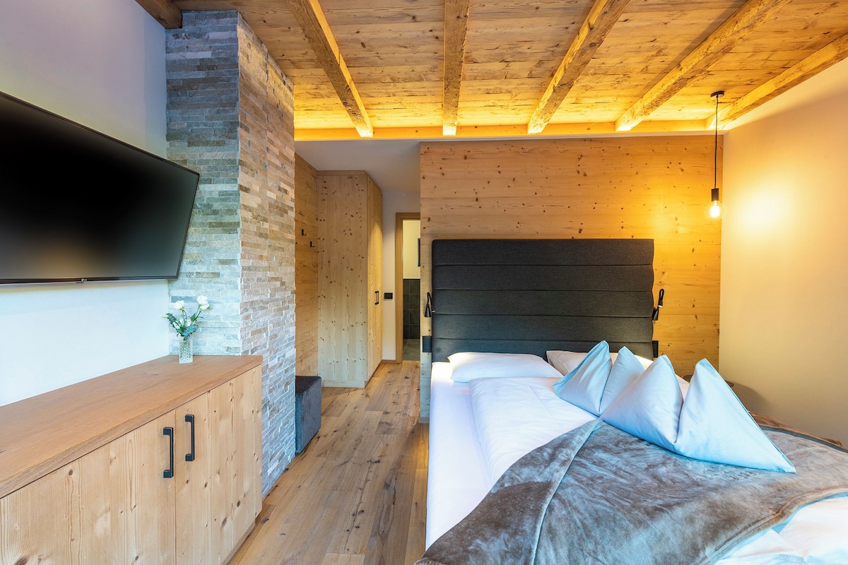 A bedroom with a bed, a wooden headboard, a TV mounted on the wall, and a wooden floor.