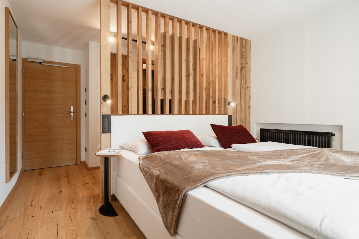 A bedroom with a wooden slat headboard, a white bed with red and white pillows, a bedside table, and a black floor lamp.