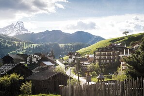 A mountain village with traditional wooden houses, a clear road, and a prominent mountain peak in the background. - Hotel Alcialc (La Valle)