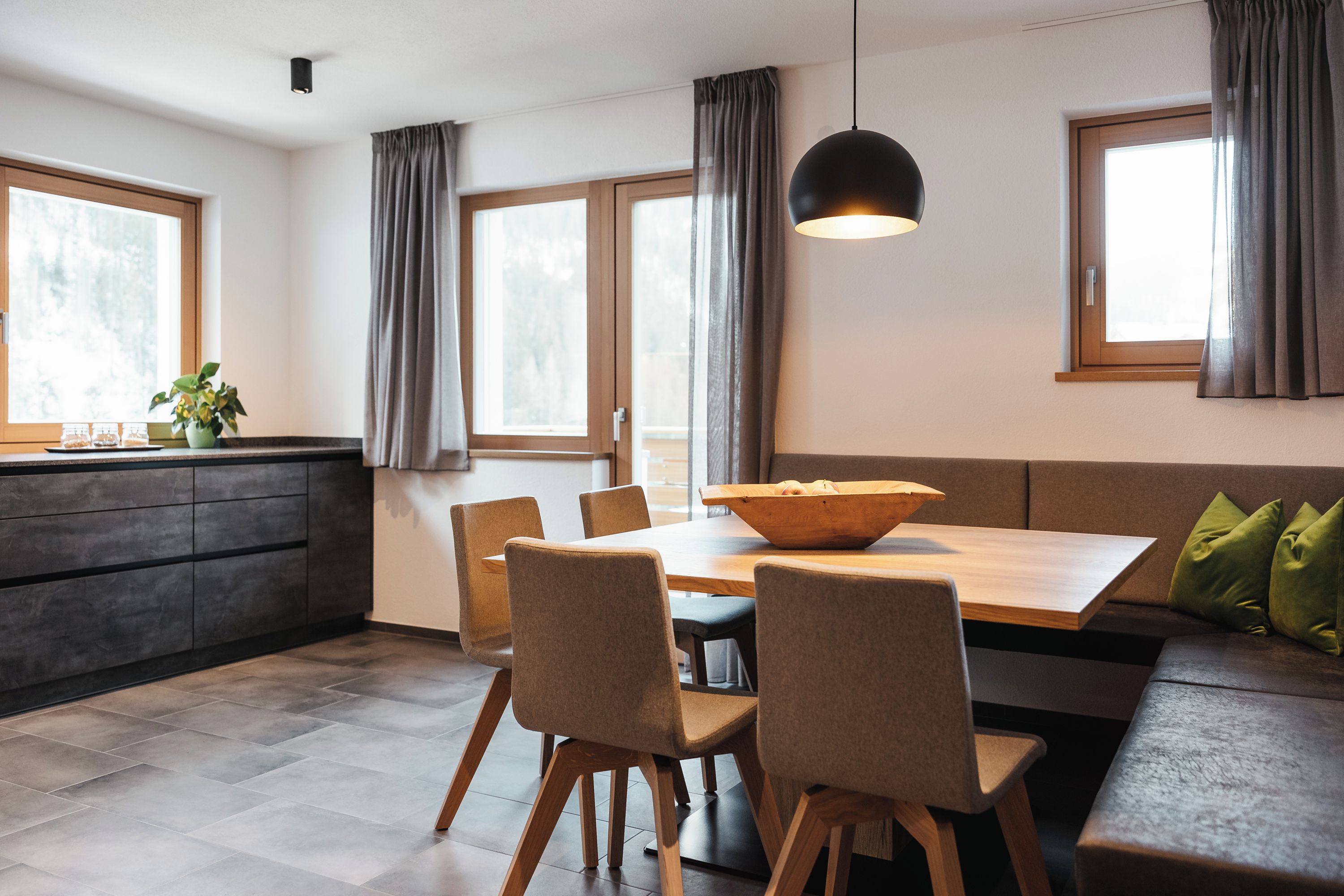 Ein stilvoller Essbereich mit Holztisch, vier Stühlen, einer Schüssel in der Mitte und einer Pendelleuchte.