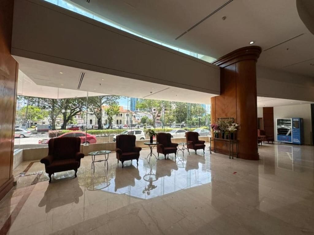 A spacious lobby with a high ceiling, a glass wall offering a view of the street, and several armchairs and tables.