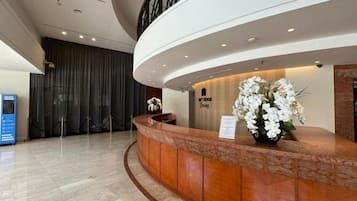 A hotel reception area with a curved reception desk, a security desk, and a staircase.