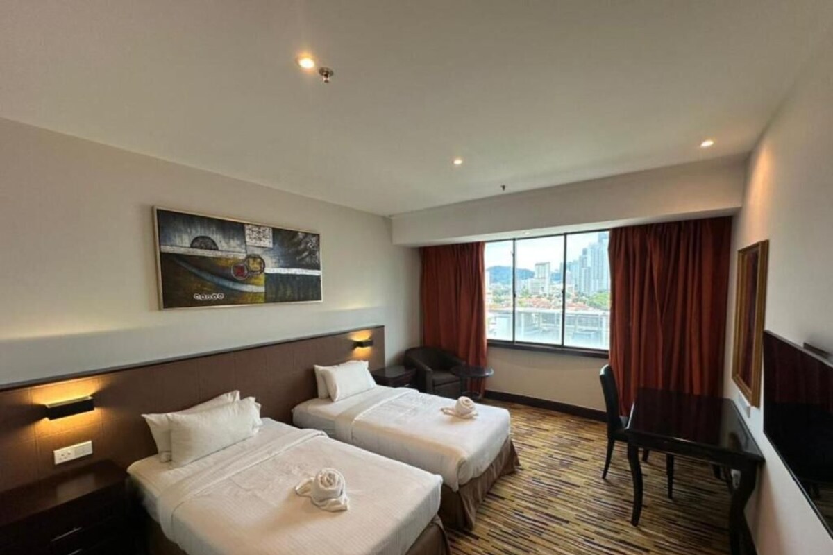 Habitación de hotel con dos camas, un escritorio, una silla, un ventanal con cortinas y un cuadro en la pared.