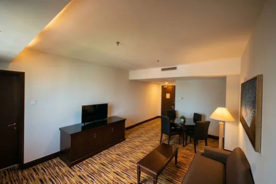 A hotel room with a flat-screen TV, a sofa, a dining table with chairs, and a lamp.