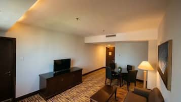 A hotel room with a flat-screen TV, a sofa, a dining table with chairs, and a lamp.