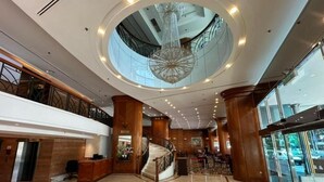Un vestíbulo amplio con una escalera central, una recepción y una gran araña.