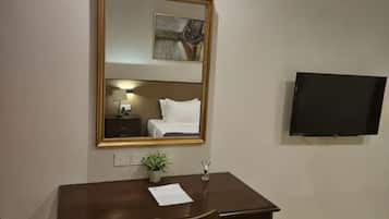 A hotel room with a bed, a desk with a chair, a television, a mirror, and a small plant.