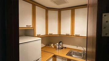 A compact kitchen with a refrigerator, sink, and wooden cabinets.