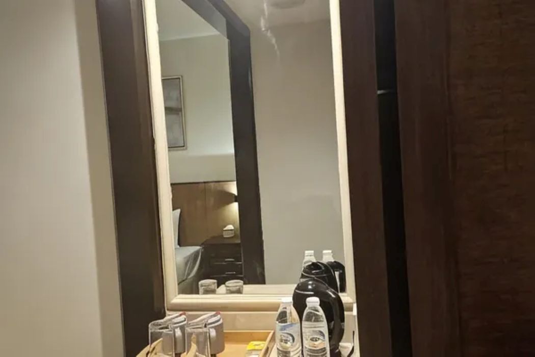 A hotel room with a large mirror, a bedside table with toiletries, and a bed.