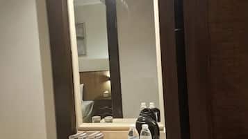 A hotel room with a large mirror, a bedside table with toiletries, and a bed.