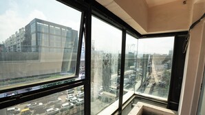 A room with large windows overlooking a busy street and a building. - Metro Stay Guest House (Barasat)