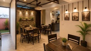 A dining area with a stone accent wall, wooden furniture, and a view of the cityscape. - Metro Stay Guest House (Barasat)