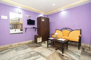 Una habitación con una pared morada, un sofá, una mesita con un florero, un armario y un televisor montado en la pared.