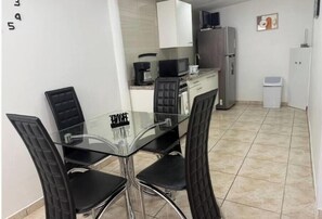 A compact kitchen with a dining table, chairs, a refrigerator, and a coffee maker. - Cozy 2-bedroom apartment near the Wendy's on the beach (Oranjestad)