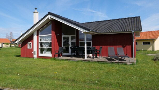 Ein rotes Gebäude mit geneigtem Dach, großen Fenstern und einer Terrasse mit Gartenmöbeln.