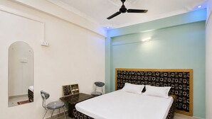 Una habitación de hotel con cama, escritorio, silla, espejo y ventilador de techo.