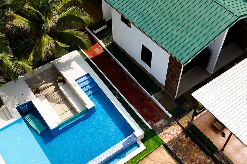 A pool with a clear blue water surface, adjacent to a building with a green roof and white walls.