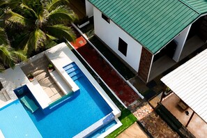 A pool with a clear blue water surface, adjacent to a building with a green roof and white walls.