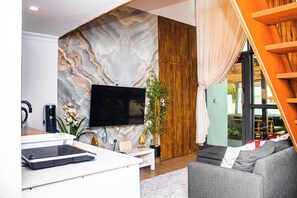 Una sala de estar moderna con un televisor de pantalla plana, una cafetera, una consola blanca, un sofá gris y un panel de pared de madera.