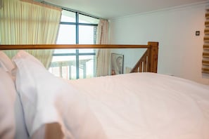 Un dormitorio con cabecera de cama de madera, un ventanal con cortinas y vistas al exterior.