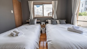 Quarto de hotel com duas camas, uma janela com cortinas, uma porta de madeira e vista para prédios.