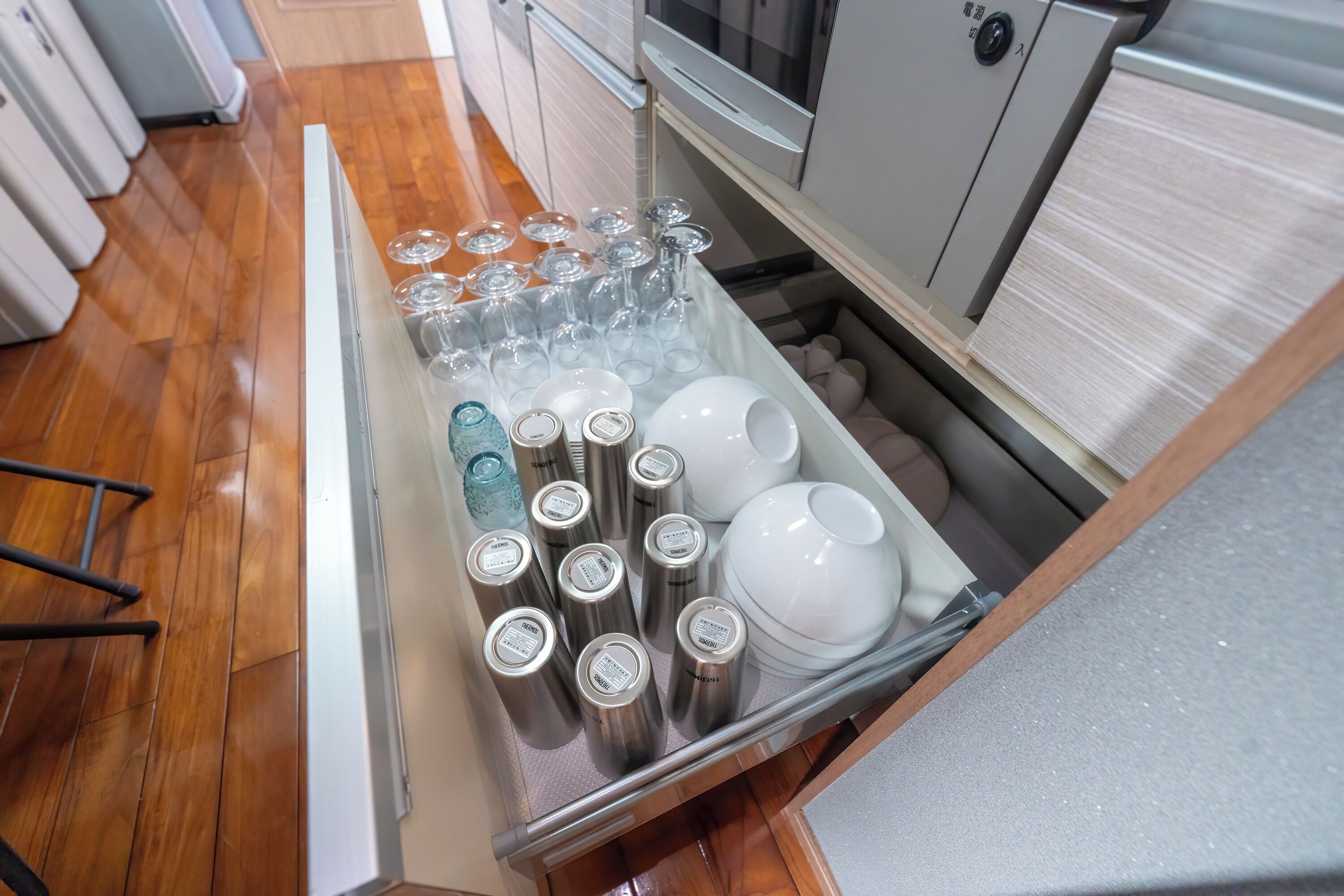 A kitchen drawer with various items including wine glasses, bottles, and dishes.