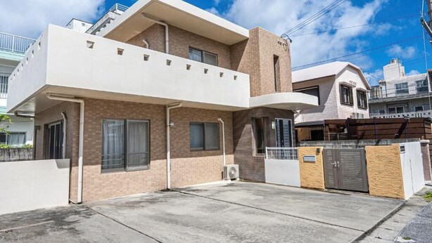 Um edifício residencial moderno com dois andares, teto plano, alpendre coberto e entrada com portão.