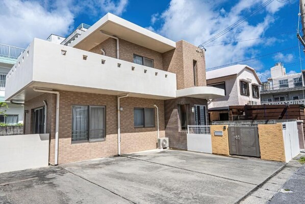 A modern two-story residential building with a flat roof, a covered patio, and a gated entrance. - Komachi House (Chatan)