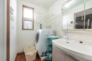 A modern bathroom with a built-in washing machine, a sink, and a mirror. - Komachi House (Chatan)
