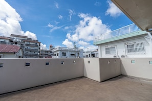 A rooftop terrace with a view of surrounding buildings and a clear sky. - Komachi House (Chatan)