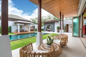 A modern outdoor patio with a pool, wicker furniture, and a clear view of a house in the background.