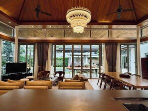 A spacious living area with a large chandelier, a television, and a dining table with chairs.