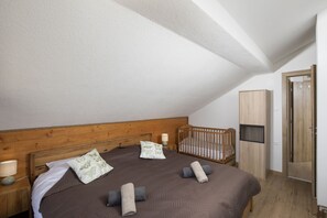 A bedroom with a wooden headboard, a crib, a wardrobe, and a bedside table with a lamp.
