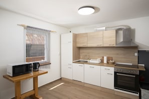 A compact kitchen with a microwave, stove, and wooden cabinets. - Villa Velebita in Lika region (Vrhovine)