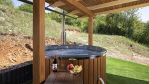 A hot tub under a wooden pergola with a bottle and a bowl of fruit beside it.