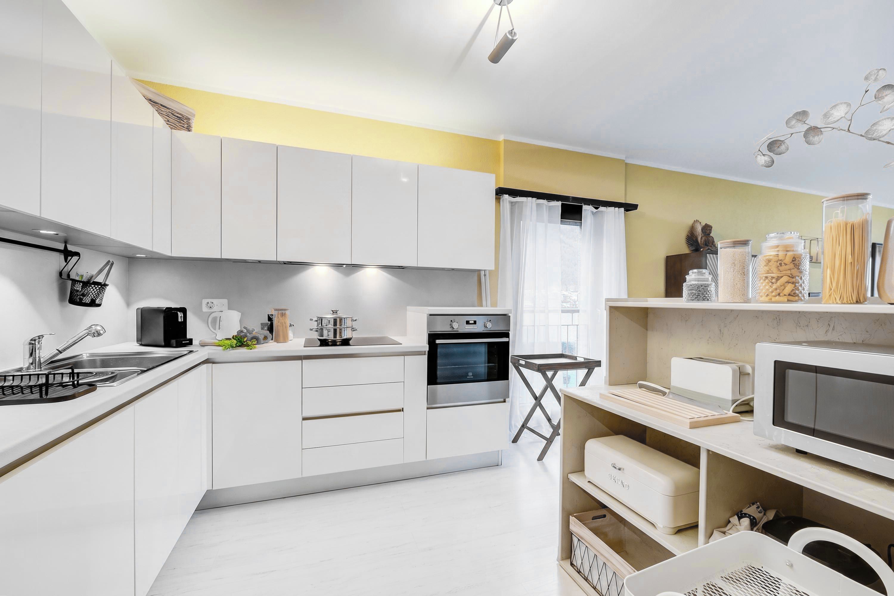 A modern kitchen with white cabinets, a built-in oven, a microwave, and a coffee maker.