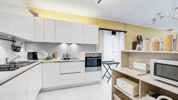 A modern kitchen with white cabinets, a built-in oven, a microwave, and a coffee maker.