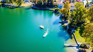 An aerial view of a lake with a boat, surrounded by buildings and greenery. - Emotion Lake Lugano With Direct Lake Access and Shared Pool (Mendrisio)