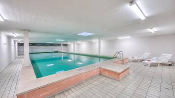 Una piscina con suelo de baldosas y un área de lounge separada con sillas.