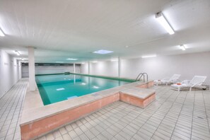 A swimming pool with a tiled floor and a separate lounge area with chairs. - Emotion Lake Lugano With Direct Lake Access and Shared Pool (Mendrisio)
