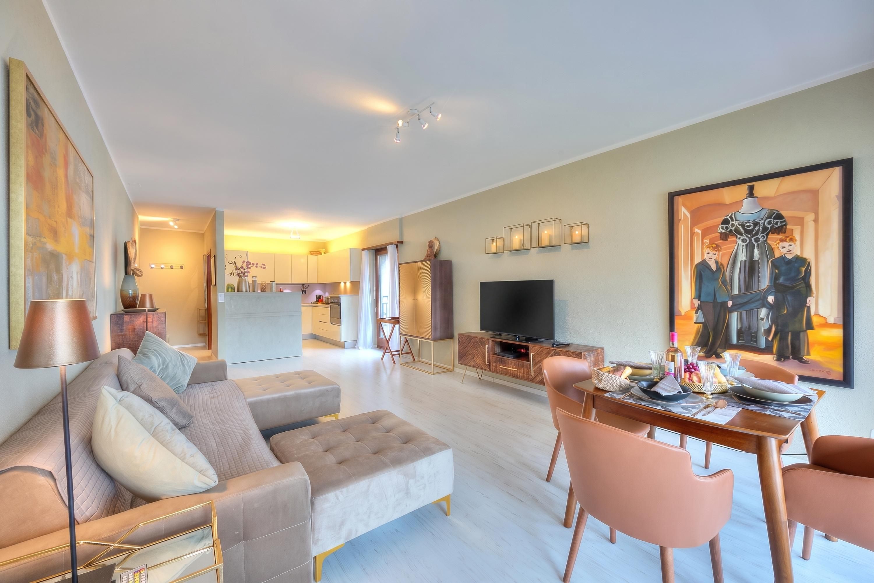 Ein modernes Wohnzimmer mit einer Couch, einem Esstisch und Stühlen, einer Küche im Hintergrund und einem Flachbildfernseher auf einer Holzeinrichtung.
