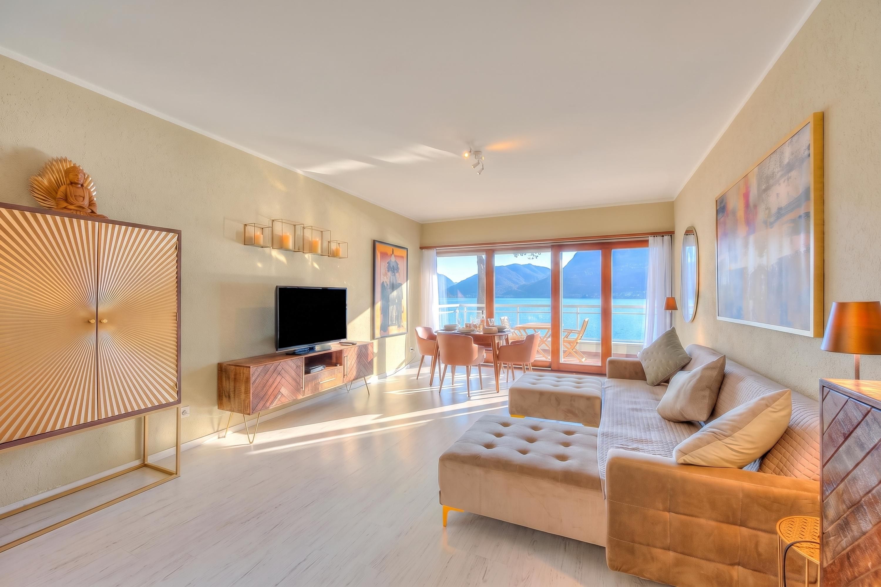 A modern living room with a sofa, television, and dining area with a view of the sea.